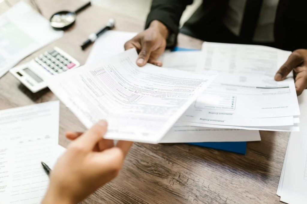 A close-up of paperwork being exchanged over a desk with a calculator in the background