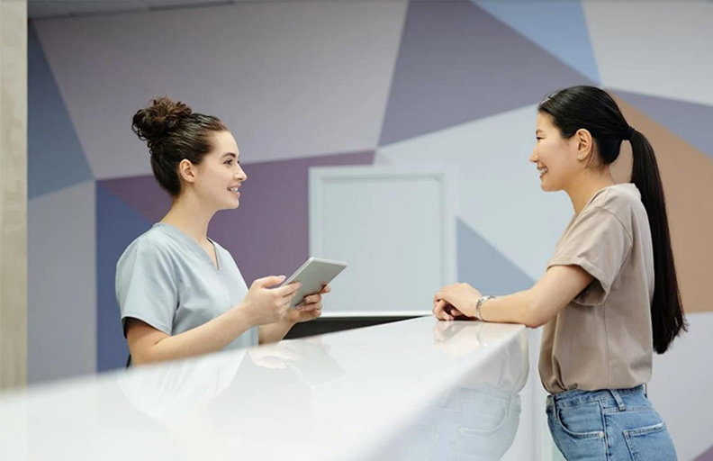 A dental nurse and patient communicating over a desk – both smiling