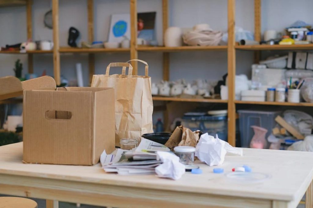 A messy public space with bags, boxes, and paper cluttered on a table.