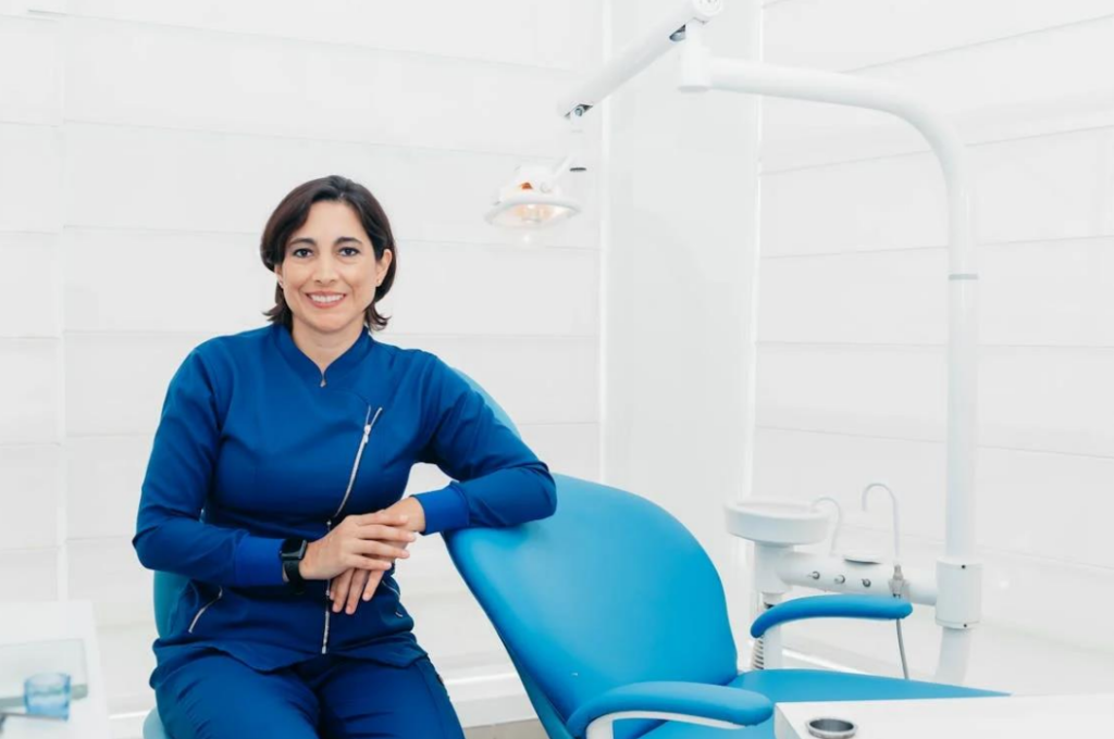 A smiling dentist with her arm resting on the dentist chair.